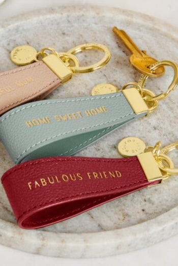 Three keychains on a marble tray with a small bottle of perfume and a card in the background.